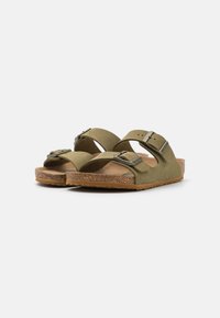 Gröna sandaler med två justerbara remmar och metallspännen, med en fotbädd av kork och en texturerad gummisula, designade för komfort.
