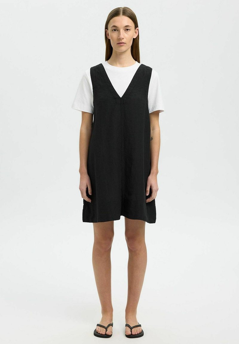 Zwarte mouwloze jurk met een V-halsontwerp, gemaakt van lichtgewicht stof, met een losse pasvorm en subtiele textuur. Draag het over een wit T-shirt.