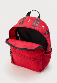 Κόκκινο υφασμάτινο σακίδιο με μαύρο εσωτερικό, μερικώς ανοιχτό κύριο διαμέρισμα, μπροστινή τσέπη με φερμουάρ, πλέγμα τσέπη στο πλάι και λαβή βρόχου στην κορυφή.