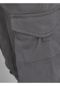 Gros plan sur une poche de pantalon cargo gris en tissu avec rabat et détails de couture visibles.