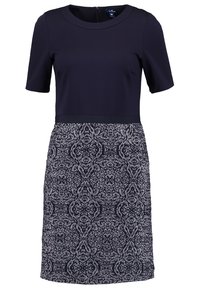 Robe bleu marine à manches courtes, col rond et taille cintrée ; la jupe présente un motif géométrique blanc et bleu marine détaillé.