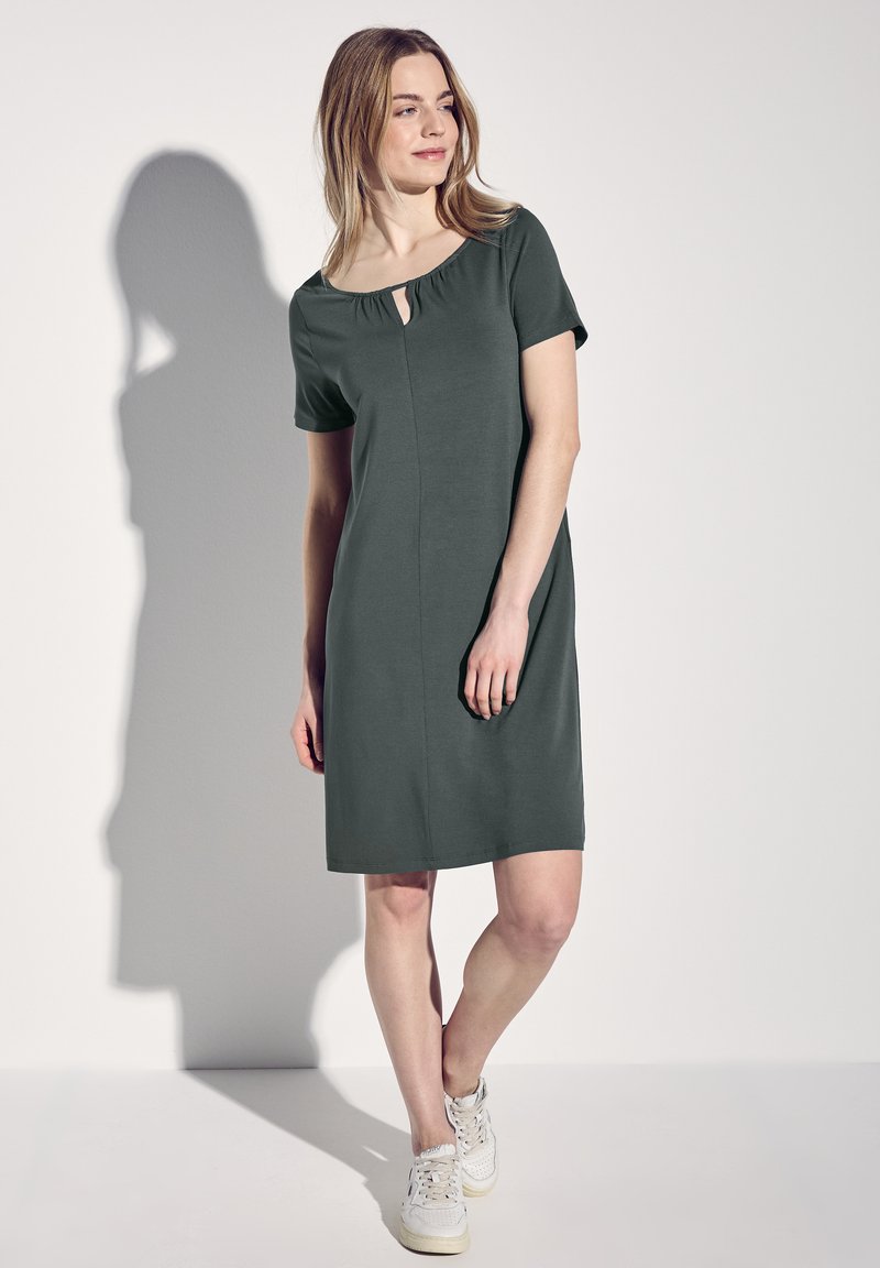 Krótka sukienka z ciemnozielonego materiału z krótkimi rękawami, wycięciem w kształcie łezki i delikatnym dekoltem. Miękki materiał, luźny krój, sięgająca powyżej kolan.