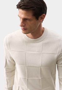 Strickpullover in Creme mit strukturiertem Quadratmuster, Rippkragen und langen Ärmeln. Hergestellt aus einem weichen, gestrickten Stoff für angenehmen Tragekomfort.