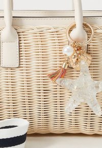 Borsa intrecciata in paglia color crema con finitura testurizzata, caratterizzata da un charm dorato con una stella marina e dettagli a nappine colorate.