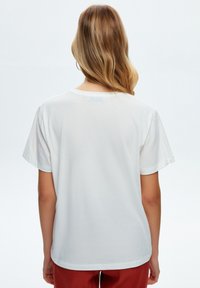 Camiseta de algodón blanca con un corte relajado, mangas cortas y escote redondo, que cuenta con una textura suave y un diseño liso en la parte posterior.