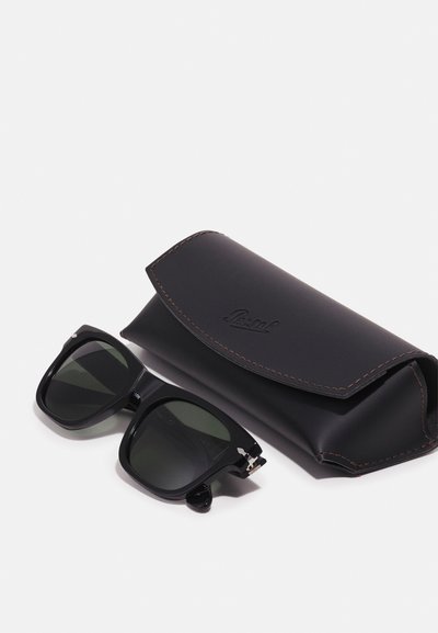 Sorte solbriller med mørke linser, rektangulær form og metallakenter ved siden av et svart lædderetui med sømdetaljer og logo.