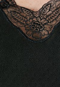 Top nero con scollatura a V, caratterizzato da un intricato bordo in pizzo nero e motivi floreali. Tessuto a coste con piccoli dettagli in rilievo sparsi.
