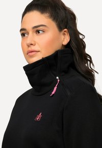 Zwarte sweatshirts met hoge hals, voorzien van een ritskraag met een roze trekkoord, en een klein roze logo geborduurd op de borst.