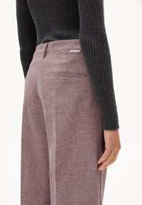 Hooggeprijsde mauve broek in een textuurstof, met een achterzak en een discreet logotag, gecombineerd met een donkere geribbeldetrui.