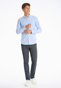 Lichtblauw overhemd met lange mouwen, gecombineerd met donkergrijze broek en witte sneakers. Het overhemd heeft een subtiele textuur en kraag.