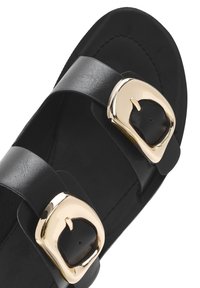 Sandalia de cuero negro con dos correas anchas y hebillas doradas. La plantilla es suave y la forma general es plana y descubierta.