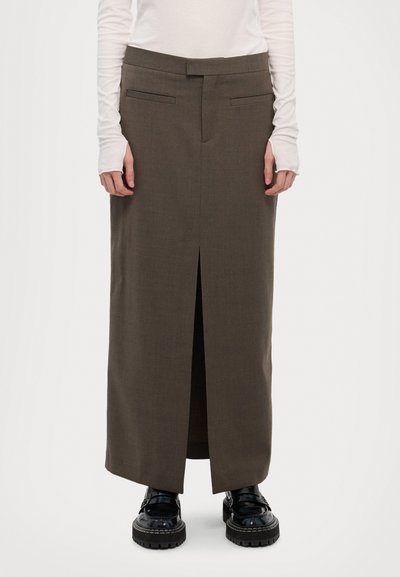 Barna, hosszú szoknya, elöl hasítékkal, texturált anyagból készült. Két oldalsó zsebbel és lapos derékpánttal rendelkezik. Fekete platform cipőkkel van viselve.