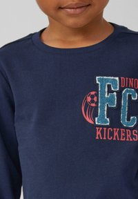 Dunkelblaues Sweatshirt mit Rundhalsausschnitt, das mit strukturiertem blauen und roten Schriftzug "FC Kickers" und einem Fußballgrafik versehen ist.