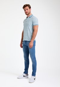 Camiseta polo de color azul claro con mangas cortas, tejido texturizado, con un cuello y ribetes de mangas en contraste, combinada con unos jeans azul claro y zapatillas blancas.