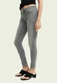 Jeans de mezclilla gris de corte ajustado con una cintura de altura media, que presentan una ligera textura desgastada. Combinados con sandalias negras tipo slides.