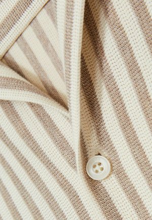Tejido de punto a rayas en beige y crema, con cierre de botón. La textura es de punto suelto con patrones de costura visibles.