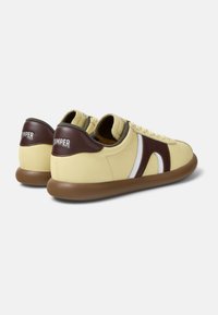 Snörskor i gult läder med bruna detaljer, vit sidrand och gummisula. Texturerad brun hälpanel med varumärkeslogga.