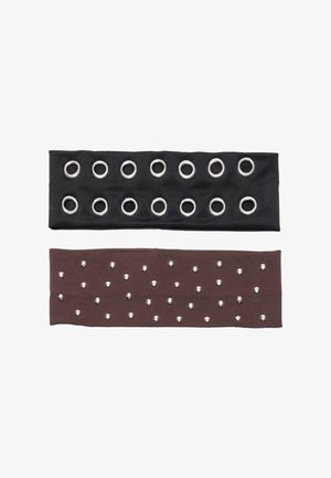 Dwie opaski na głowę z tkaniny: jedna czarna z metalowymi srebrnymi oczkami, druga brązowa z srebrnymi ćwiekami, obie płaskie i elastyczne.
