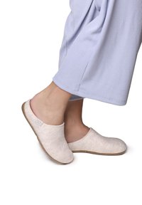 Filttofflor i ljusbeige med en böjd form, en gummisula och minimala sömnadsdetaljer, bärs med ljusblå vida byxor.