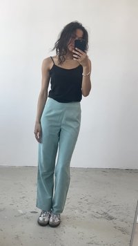 Svart ermeløs topp sammen med lyse teal høyt midje bukser. Modellen har på seg grå og svarte sneakers. Speilrefleksjon vises.