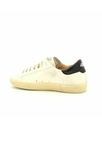 Sneaker di pelle bianca con un tallone nero, punta rotonda e suola in gomma beige. Presenta lacci piatti e piccoli fori di ventilazione sui lati.