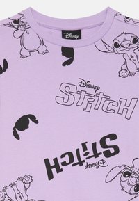 Svetlofialové tričko s čiernymi kreslenými postavičkami, vrátane Stitche, a odvážnym textom "Disney STITCH" s hravými dizajnmi po celom tričku.