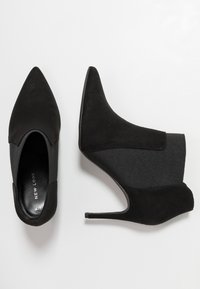 Schwarze Stiefeletten mit spitzer Zehenpartie, aus Wildleder, mit elastischen Seitenpaneelen und hohen Stiletto-Absätzen. Glatte und strukturierte Oberflächen.