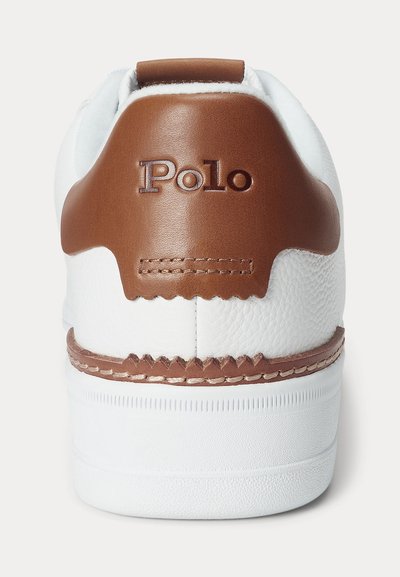 Toc alb de sneaker cu o bucățică de piele maro cu marca „Polo” și cusături maro detaliate deasupra tălpii albe de cauciuc.