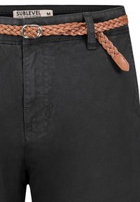 Schwarze Hose mit geflochtenem braunem Leder-Gürtel und silberner Schnalle. Glatte Textur mit klassischem Design und minimalen Nahtdetails.