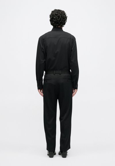 Μαύρο πουκάμισο με μακριά μανίκια σε συνδυασμό με μαύρο παντελόνι, με εφαρμοστή γραμμή και ομαλή υφή. Η εμφάνιση διαθέτει τσέπες στην πλάτη και απλό στυλ.