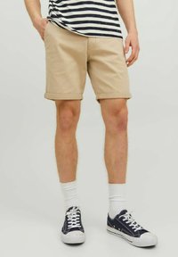 Beżowe bawełniane szorty z podwiniętymi nogawkami, noszone z białymi skarpetami i granatowymi płóciennymi butami, w połączeniu z pasiastą granatowo-białą koszulą.