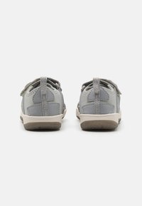 Graue Stoffschuhe mit einer weichen, strukturierten Oberfläche. Merkmale sind elastische Schnürsenkel, eine Zuglasche an der Rückseite und eine leichte gummierte Sohle in Beige.