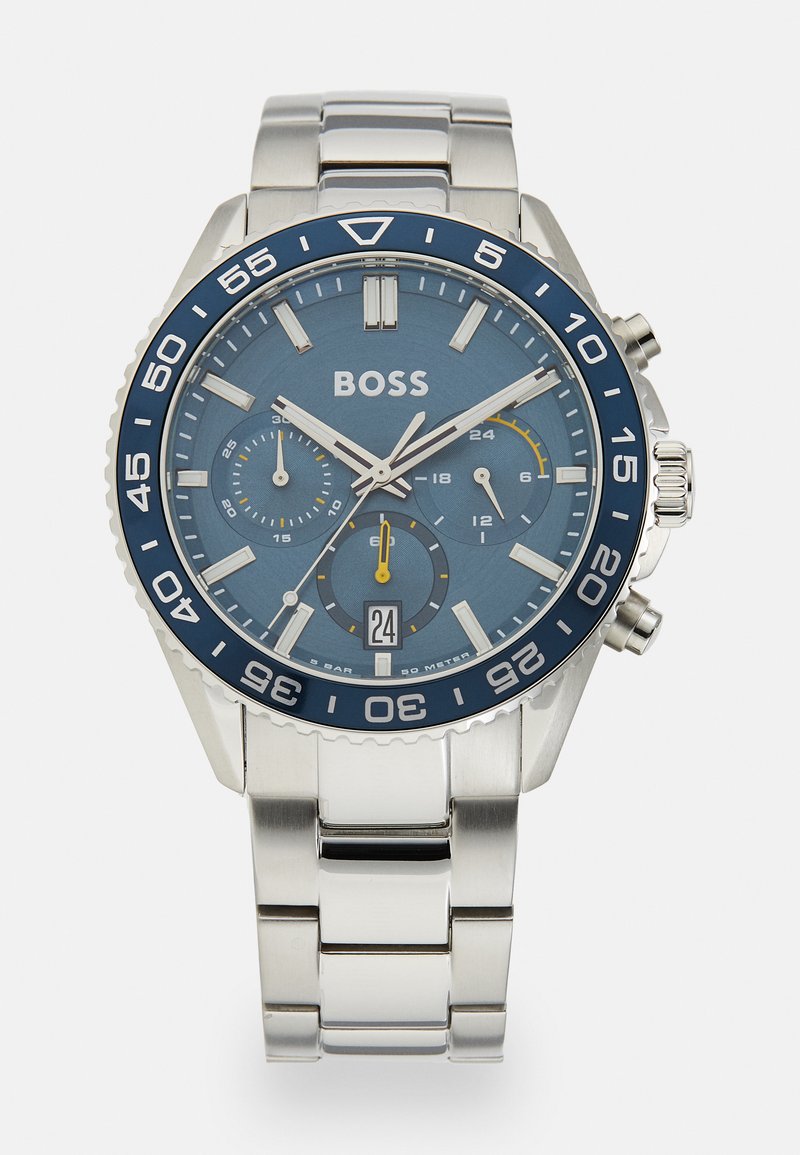 Orologio in metallo argentato con quadrante blu. Presenta indici delle ore argentati, sottodial della cronografo, visualizzazione della data e un bezel blu. Bracciale in acciaio inossidabile.