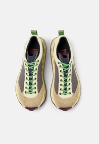 Sportovní tenisky s béžovým a šedým pleteným svrškem, zelenými tkaničkami a texturovanou gumovou podrážkou. Logo je viditelné na jazyku.