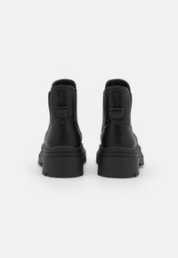 Para czarnych skórzanych botków za kostkę z masywnymi podeszwami, widocznych z tyłu na jednolitym białym tle.