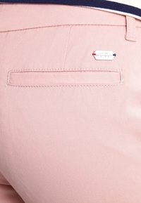 Pantaloni in cotone rosa con una tasca posteriore e un'etichetta con logo. Tessuto morbido, design slim fit e dettagli cuciti.