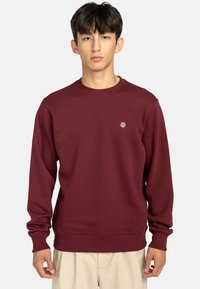 Bordeaux sweatshirt lavet af blødt stof, med runde halsudskæring, lange ærmer og et lille logo på brystet. Enkel design, ingen mønstre.