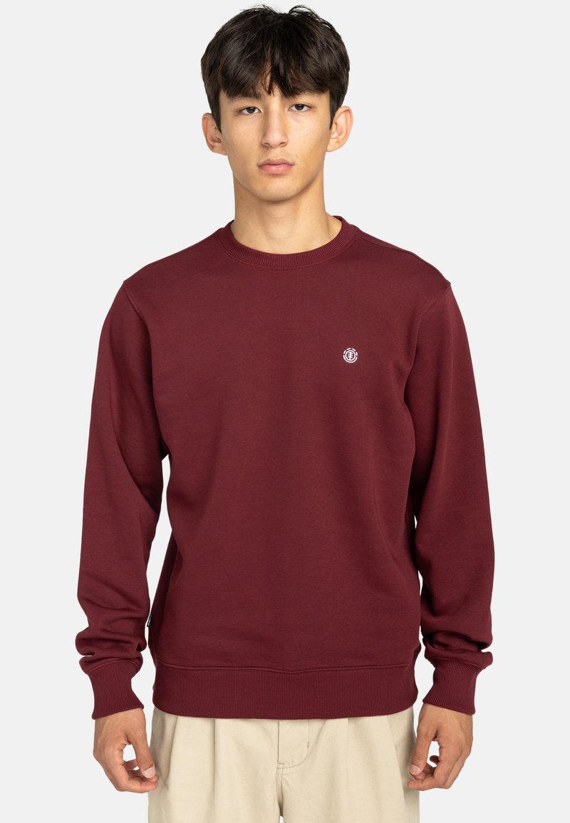 Bordeaux sweatshirt lavet af blødt stof, med runde halsudskæring, lange ærmer og et lille logo på brystet. Enkel design, ingen mønstre.