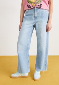 Light blue high-waisted jeans in a wide-leg cut with a raw hem, paired with mint green sneakers. T-shirt features a colorful floral design.