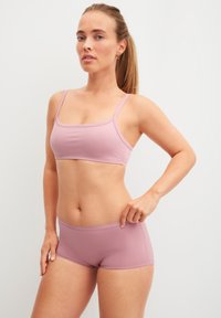 Lichtroze naadloze bralette met dunne bandjes en bijpassende high-waisted shorts. Glad oppervlak en aansluitend ontwerp. Minimalistische stijl.