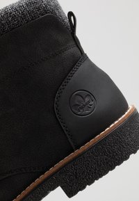 Bottine noire à la cheville avec une tige texturée, des accents en cuir lisse, un emblème rond, et une semelle en caoutchouc avec une finition texturée.