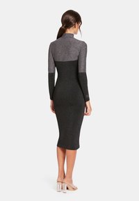 Robe à manches longues noire et argent, avec une silhouette ajustée et une longueur mi-mollet, présentant un col haut et des détails de paillettes discrètes.