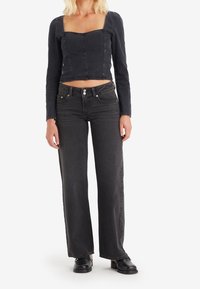 Czarny dżinsowy crop top z długim rękawem i kwadratowym dekoltem, w zestawieniu z czarnymi spodniami o wysokim stanie i prostych nogawkach, które mają pięć kieszeni i zapięcie na guzik.