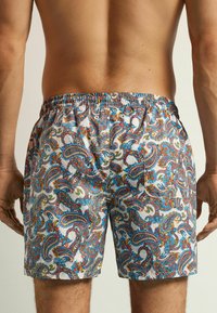 Bañadores para hombre con un colorido estampado de paisley en tonos de azul, rojo y amarillo; cinturilla elástica con cordón y bolsillos laterales.