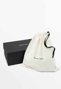 Sac en coton à cordon en crème avec des accents noirs, affichant "Massimo Dutti" imprimé, aux côtés d'une boîte rectangulaire noire.