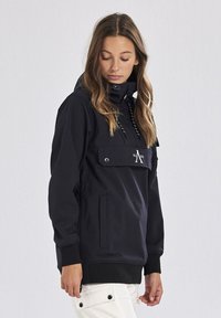 Svart pull-overjacka med en framficka, justerbar huva och elastiska ärmslut. Slät textur och dragsnöre-accenter ökar funktionen.
