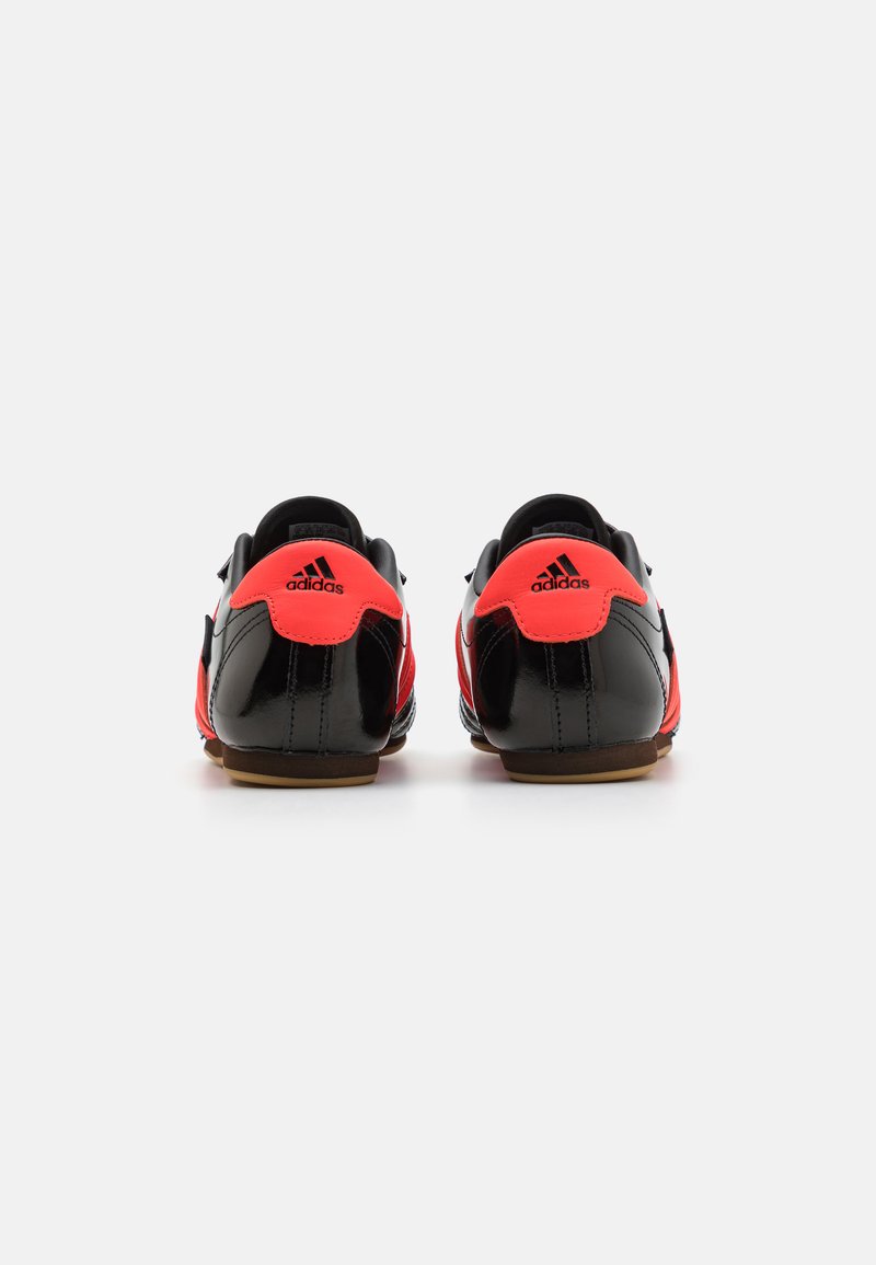 Zapatillas deportivas negras y rojas con un acabado brillante, que cuentan con un diseño de perfil bajo, acentos texturizados y una suela de goma para mayor tracción.