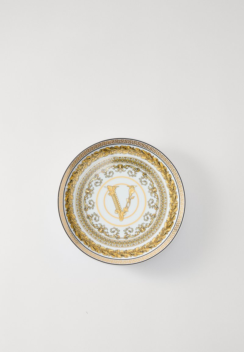 Balts porcelāna šķīvis ar sarežģītiem zelta un ziliem ziedu rakstiem, centrā atrodas emblēma un dekoratīva grieķu atslēgas apmale.