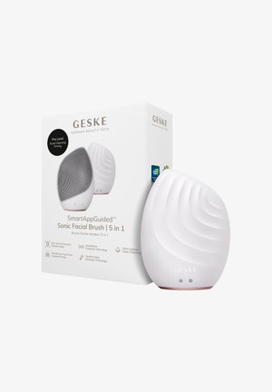 Witte, ovaalvormige GESKE sonische gezichtsborstel met gestructureerd oppervlak naast de doos die de 5-in-1 functies en slimme app-geleiding benadrukt.