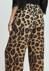 Pantalons à large jambe en imprimé léopard dans une palette de couleurs beige et noir, avec une taille élastique et un tissu doux et texturé.
